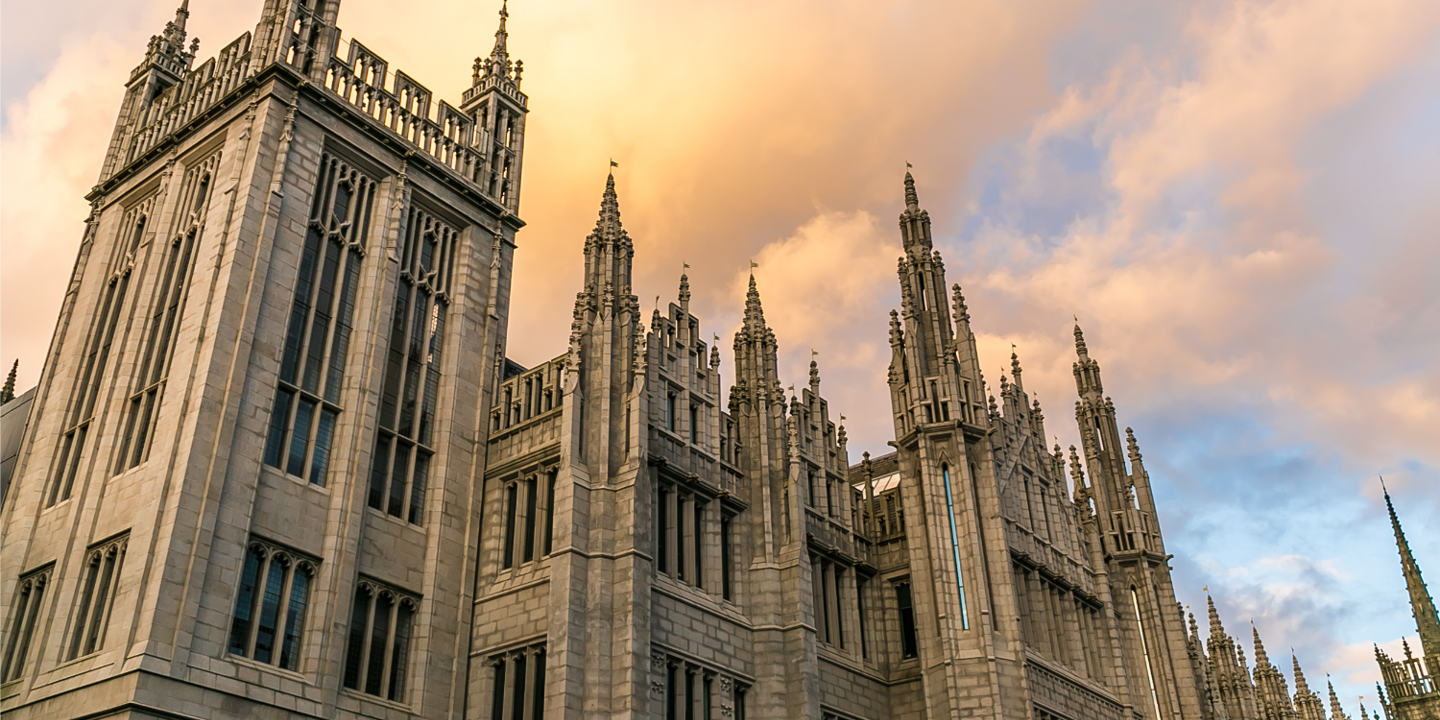 A view of Marischal College taken from a low angle and looking towards the sky. The roof parapets and architecture of this stone building are prominently featured.