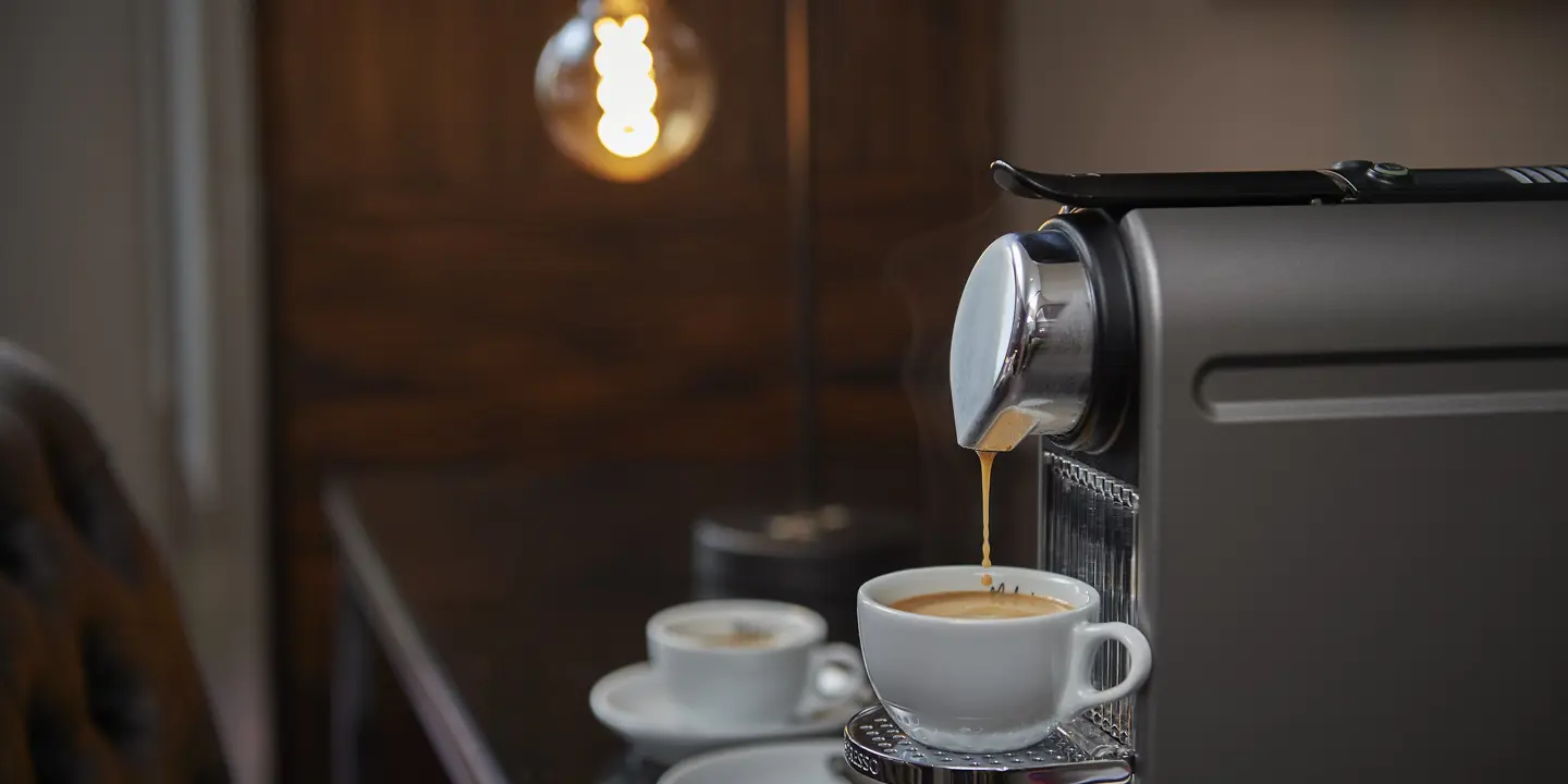 A cup of coffee being poured by a coffee machine.