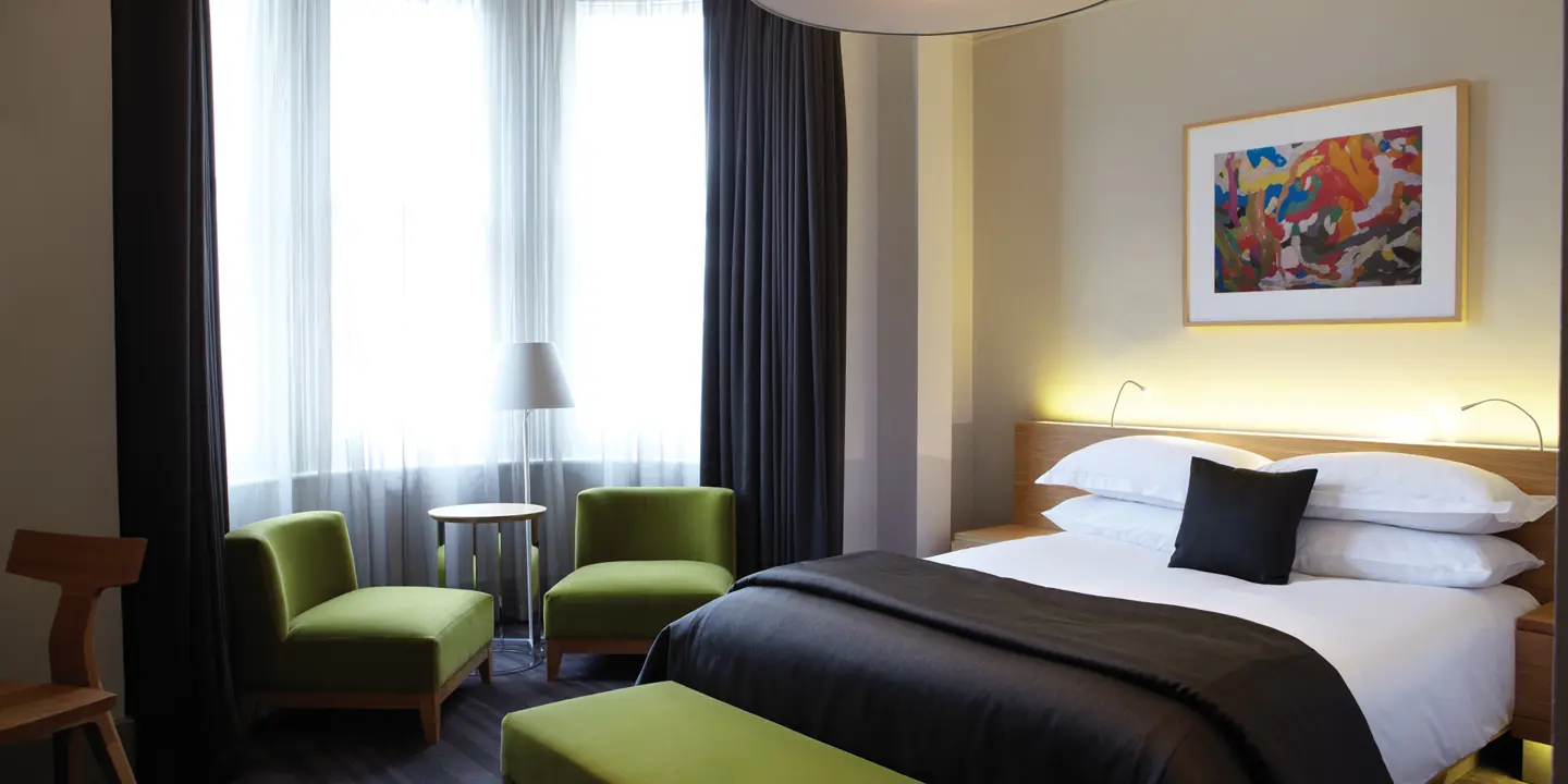 An elegantly furnished hotel room featuring a comfortable bed, two armchairs and a table.