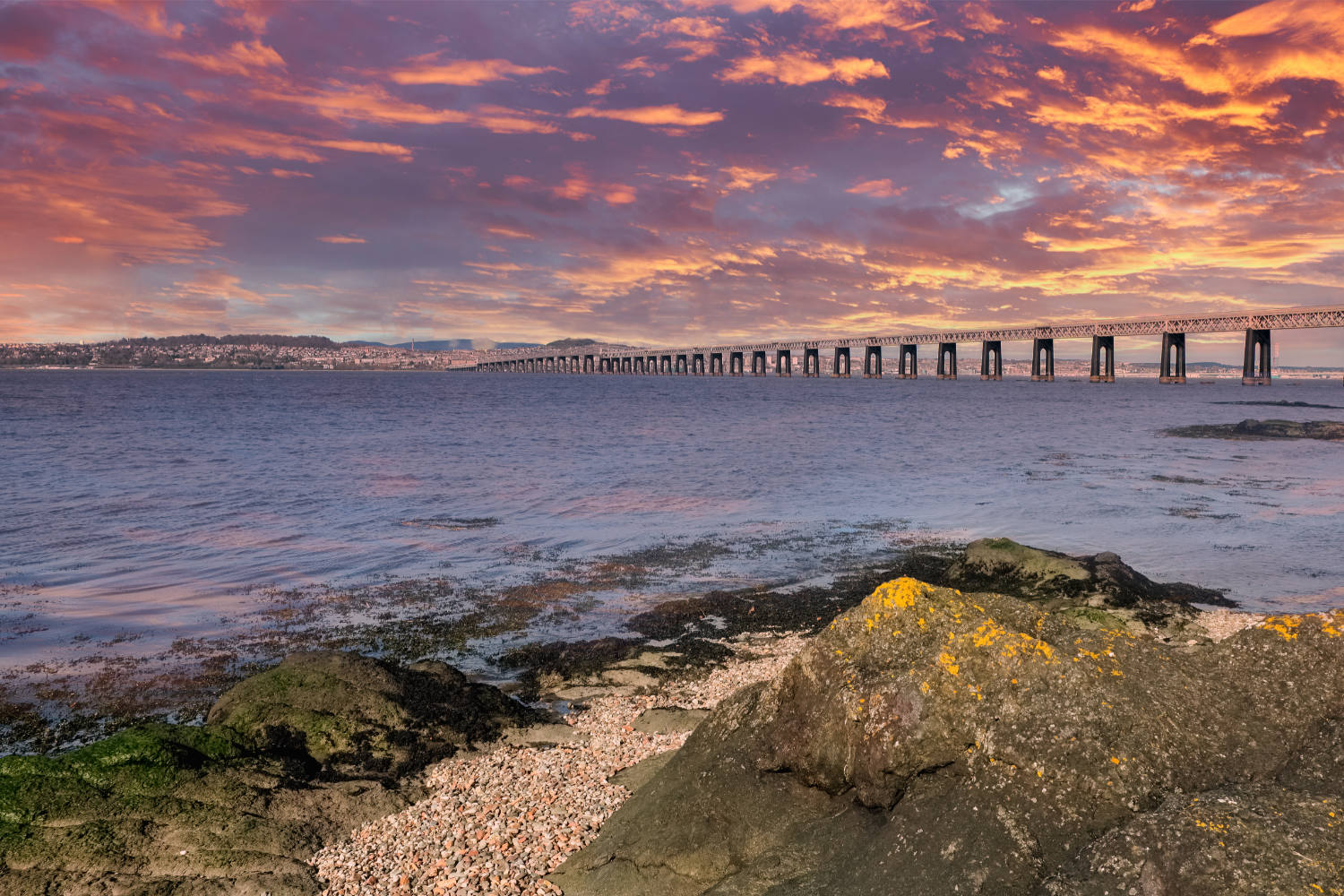 Scenic view of a serene ocean sunset with a bridge in the background.