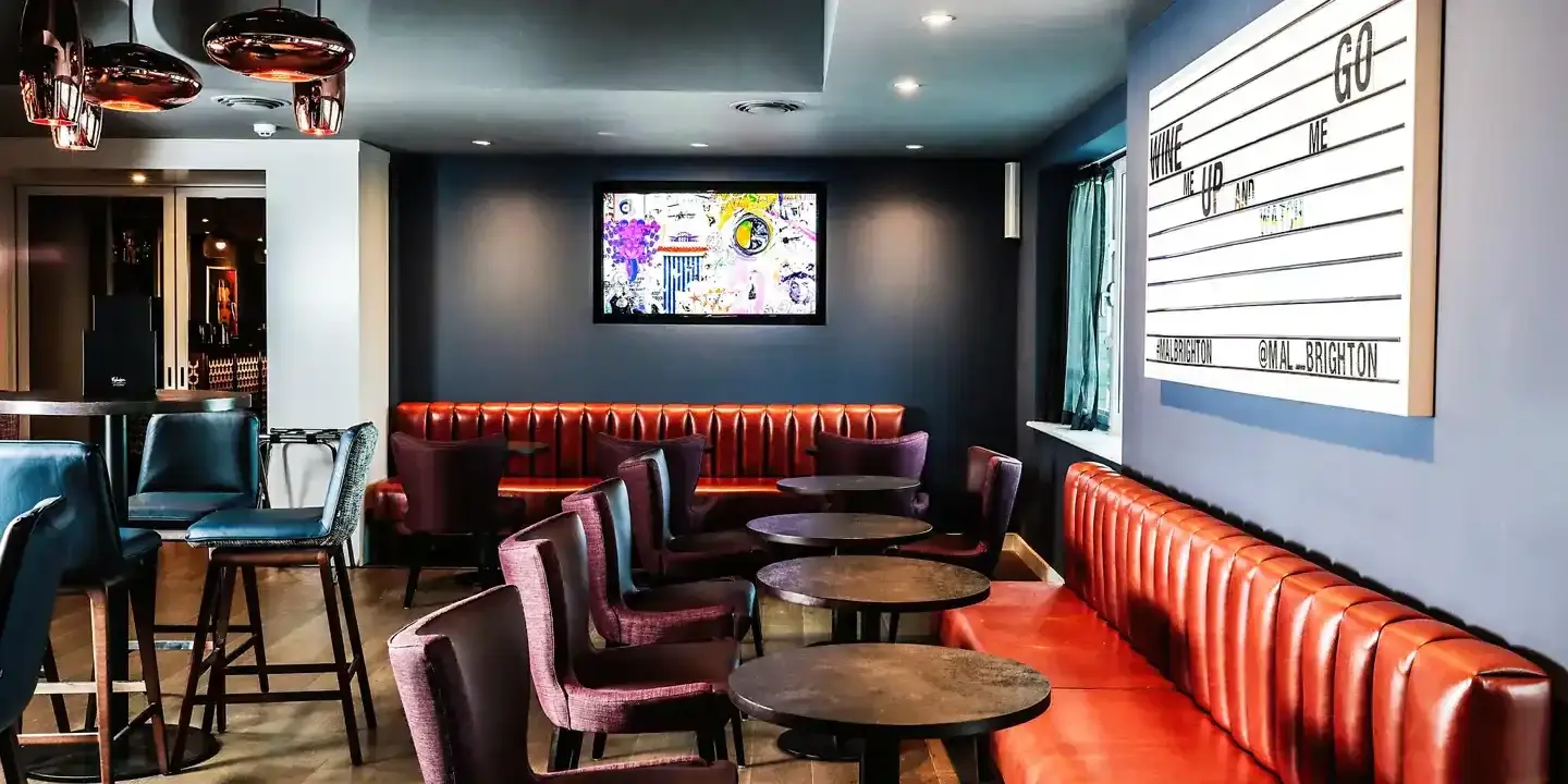 Bar featuring leather bench seats, tables, stools, brass lighting and a wall-mounted television.