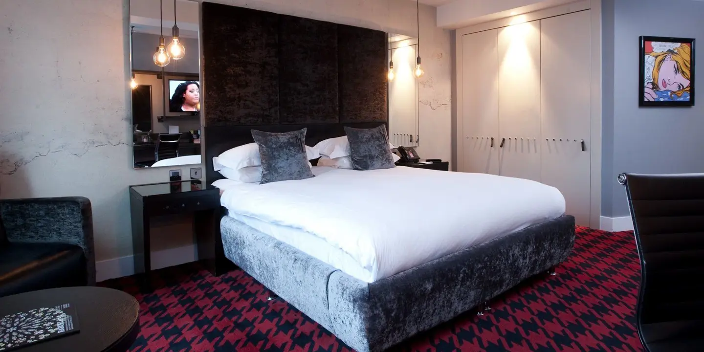 View of the double bed in the standard room. Red houndstooth carpet is visible and there are mirrors either side of the bed and pop art  adorning the walls.