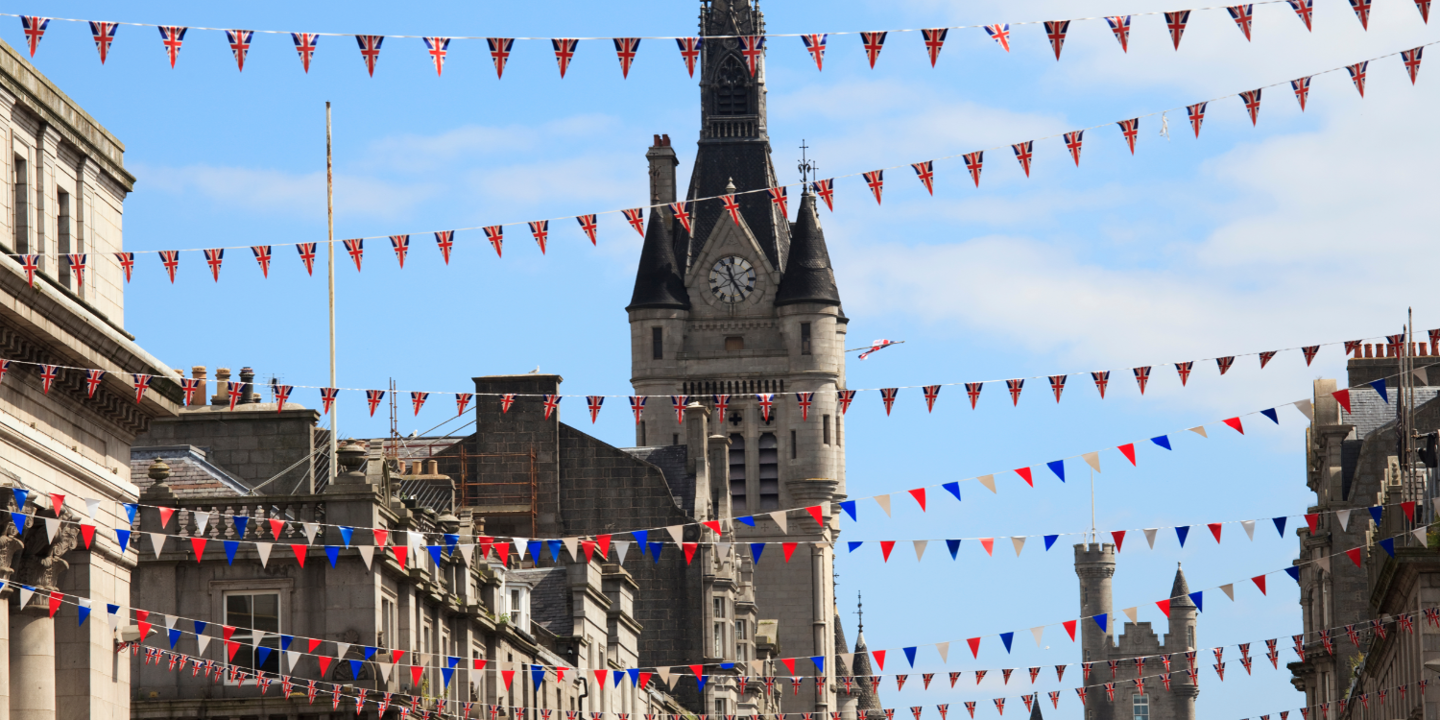 Union Jack bunting stretches across a street in Aberdeen, in the background we can see historic stone build buildings including a clock tower