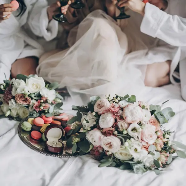 Bridesmaids sitting together on a bed with bouquets of flowers in front of them.