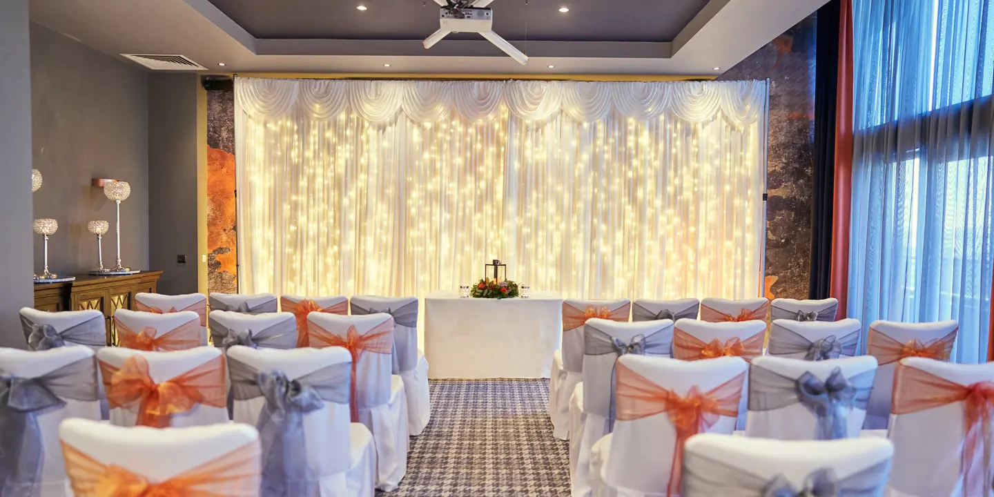 A room adorned with chairs draped in elegant white and orange bows.