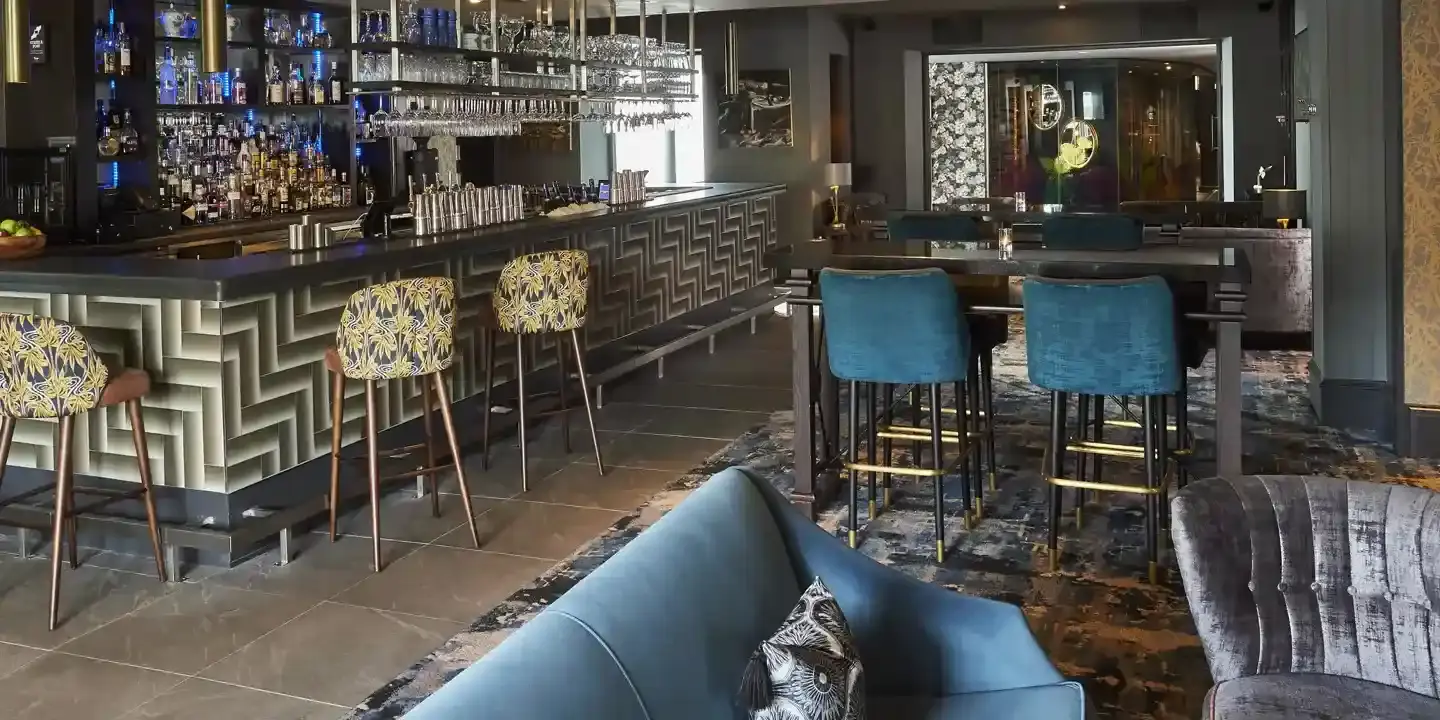 View of the bar featuring numerous blue chairs and yellow patterned fabric stools arranged along a bar counter.