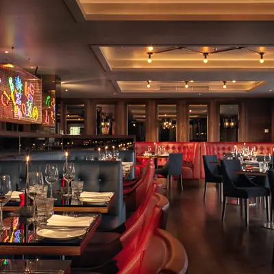 Birmingham Malmaison restaurant interior alternate view showing red leather seating including booths. A feature neon sign with multiple colours is visible on one wall. 