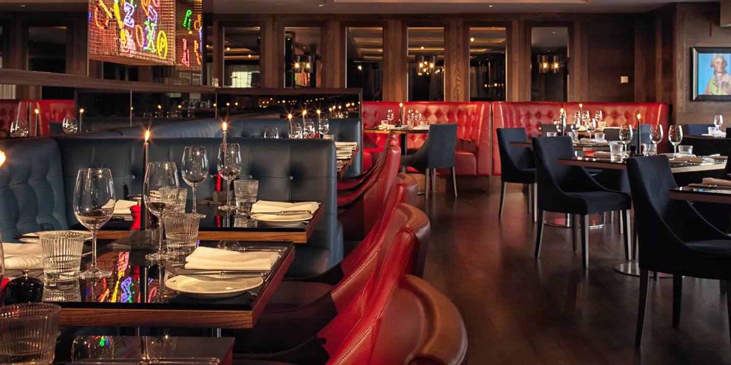 Birmingham Malmaison restaurant interior alternate view showing red leather seating including booths. A feature neon sign with multiple colours is visible on one wall.