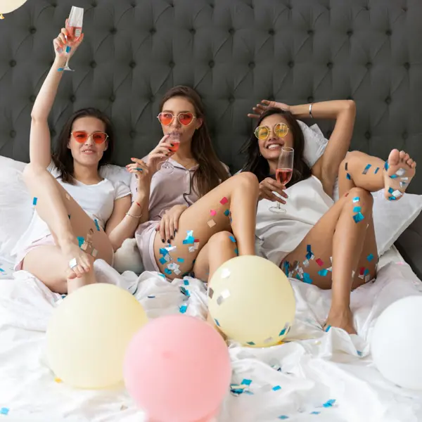 Three women laying on a bed with confetti and balloons 