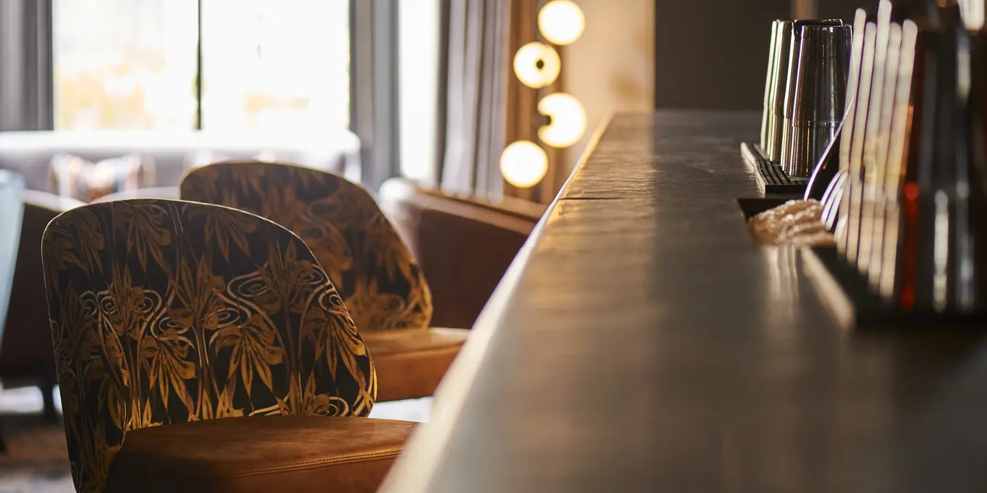 Patterned fabric stools arranged neatly alongside a bar counter, with warm lighting out of focus in the background.