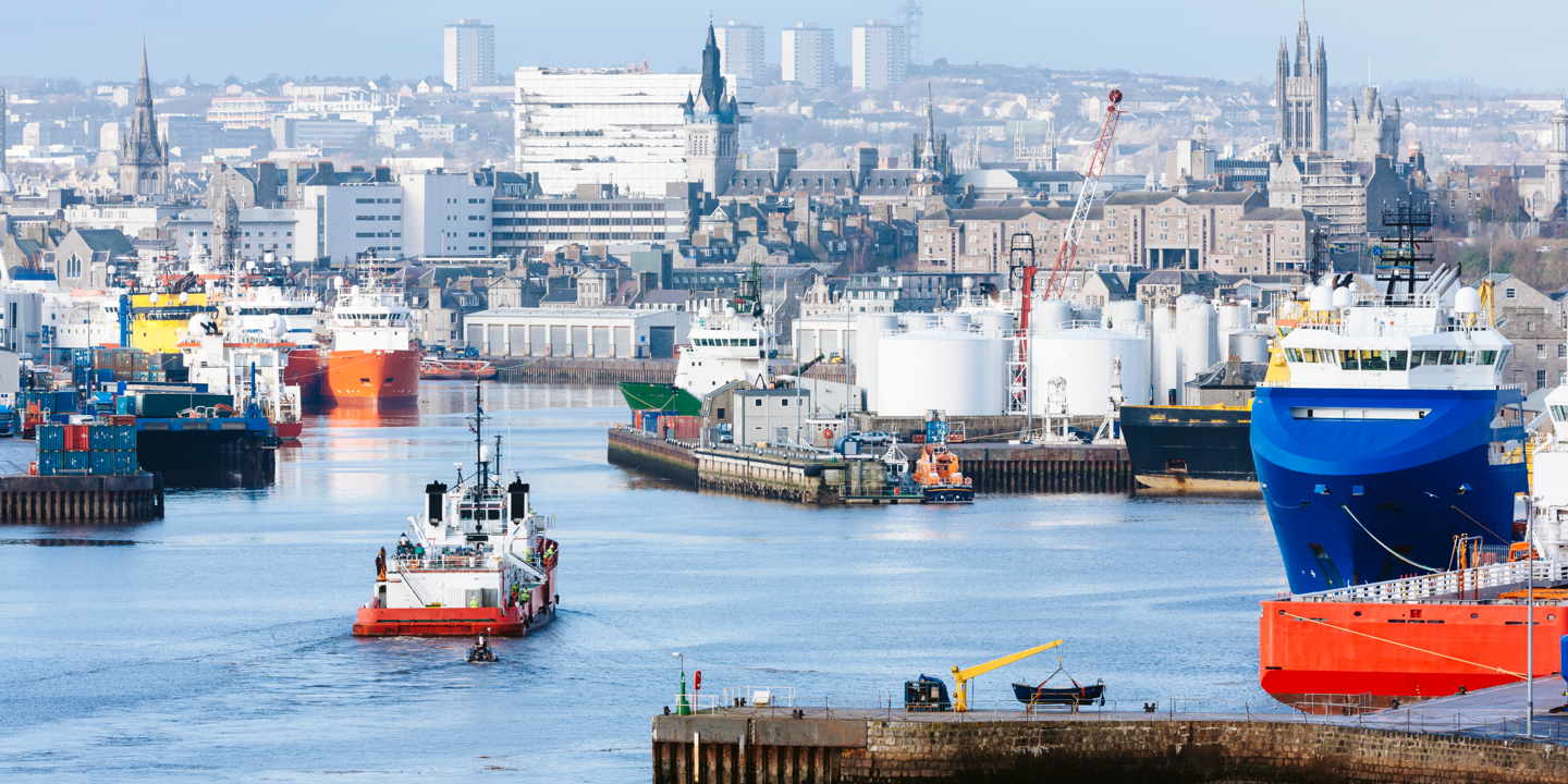 A view of Aberdeen harbour, featuring several shipping vessels, industrial properties, and in the background the city of Aberdeen