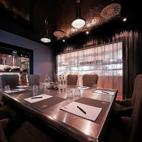 Malmaison Aberdeen Meeting room, Chef's Table. Large square table featuring 8 chairs in 2 by 2 arrangement. A large net curtain covered window looks out directly into the kitchen.