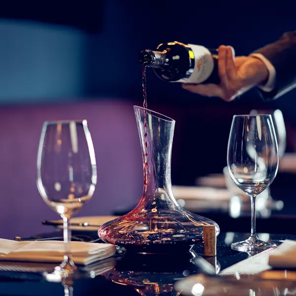 A person pouring wine into a decanter placed on a table.