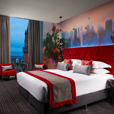 A hotel room surrounded in red decor, with a double bed in the centre