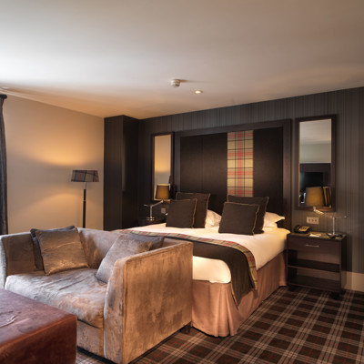 Spacious hotel room featuring a generously-sized bed with a tartan headboard.