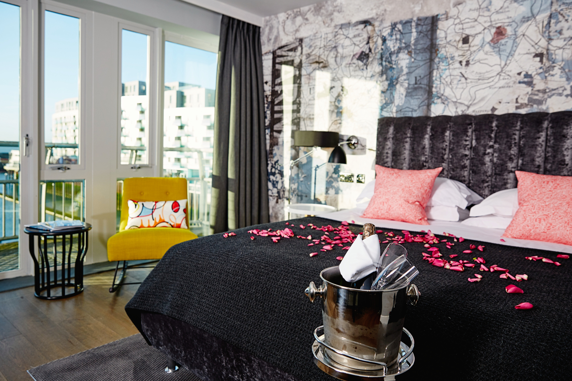 A well-furnished bedroom featuring a comfortable bed decorated with pink petals, a cozy chair, and a large window.